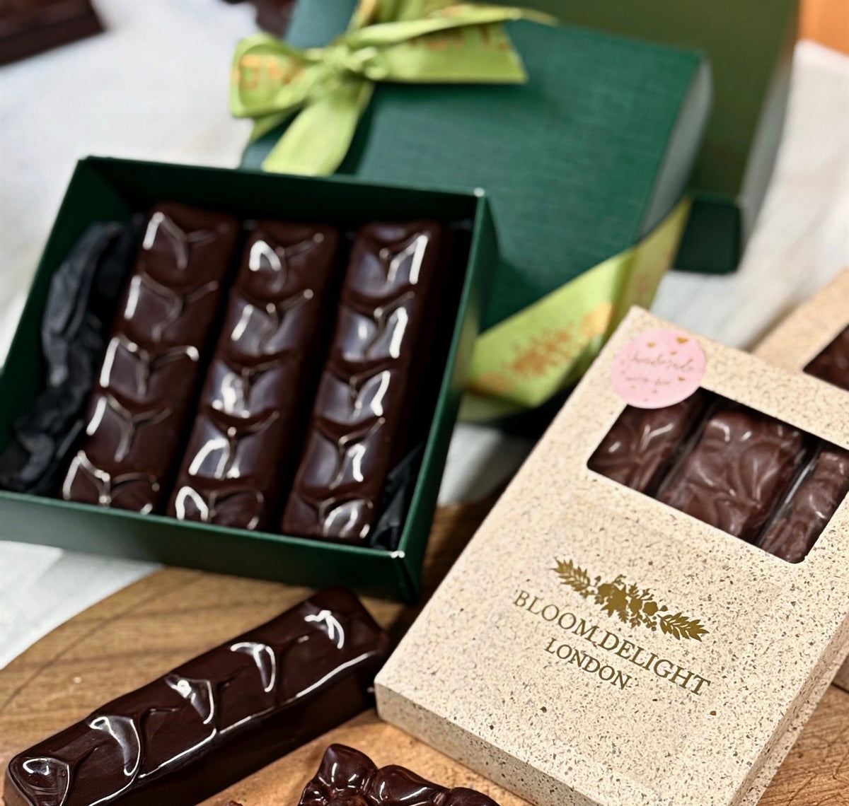 Chocolate bars in a 'Bloom Delight London' box on a wooden surface.